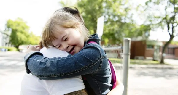 portrait of trisomie 21 child girl outside hugging his mother on a school playground